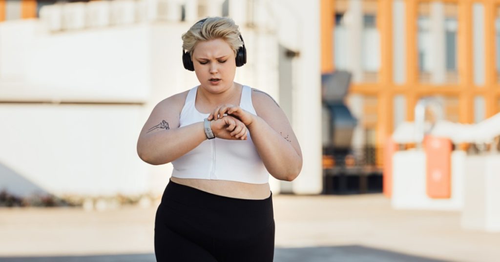 Woman in athletic clothing walking outside using her fitness tracker.