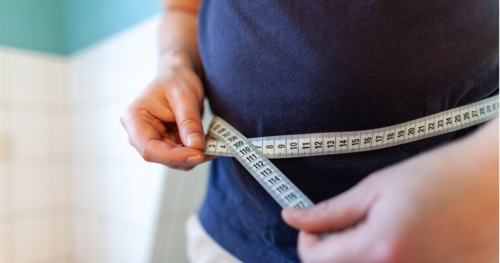 Closeup of a measuring tape wrapped around a person's stomach.