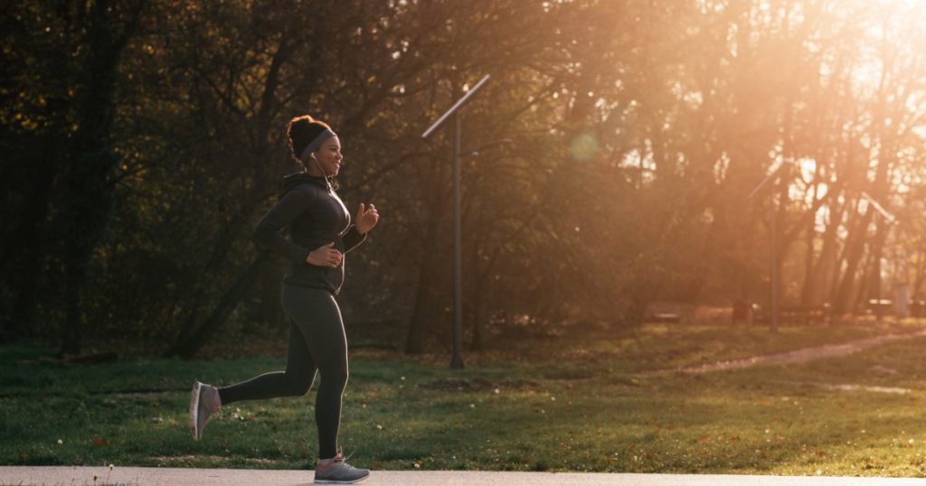 Woman running along a path in a park at sunset.