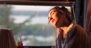 Closeup of a woman resting against a window with the sun shining on her face.