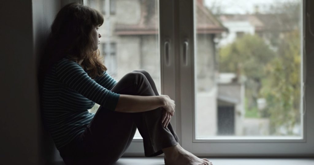 Young woman sitting on an indoor window bench, looking out the window.